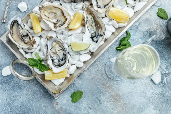 Opened oysters, ice on metal tray with lemon and ice. Restaurant menu, dieting, cookbook recipe.