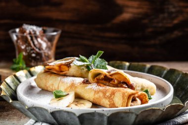 Çikolata kaplı krepler ve beyaz tabakta muz. İnce krep, blini. Lezzetli kahvaltı ya da atıştırmalık. Yemek tarifi geçmişi. Kapat..