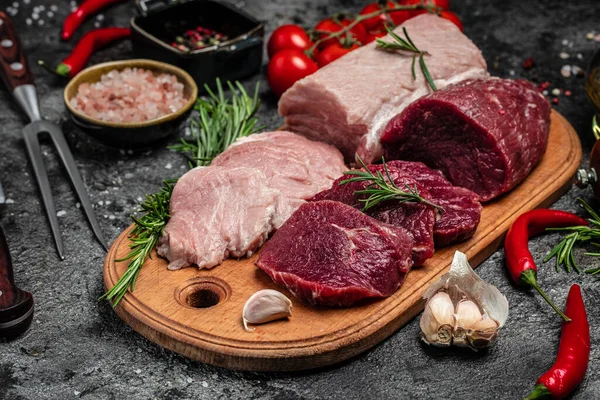 Different types of raw pork meat and beef on a dark background. various types of fresh meat pork and beef. Restaurant menu, dieting, cookbook recipe top view.