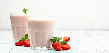 Meyveli smoothie. Çilekli smoothie ya da meyveli milkshake ve beyaz arka planda cam kavanozda yoğurt. Sağlıklı vejetaryen içeceği. Uzun afiş biçimi. en üstteki görünüm.