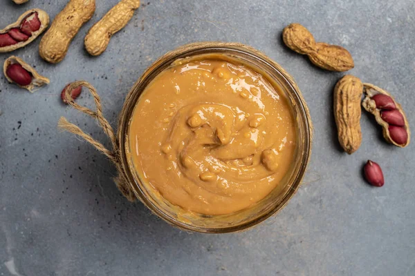Peanut butter in an open jar. creamy peanut butter peanuts scattered. top view.