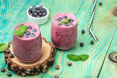 Yoğurtlu meyve suyu bardakta taze yaban mersini, nane yaprağı ve mavi arka planda çiğ bira. Restoran menüsü, diyet, yemek kitabı tarifi üst görünümü.