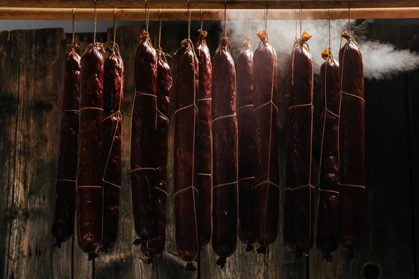 Process of smoking sausage hang in a cupboard with smoke. Clouds of smoke rise up and envelop the sausages hanging in a row. Long banner format,