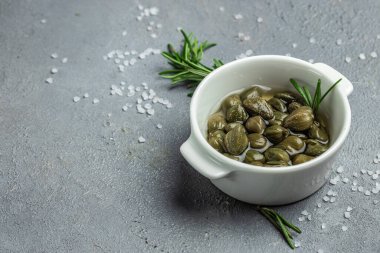 Hafif ahşap arka planda, küçük bir kasede taze biberiyeyle marine edilmiş kapari. Uzun afiş biçimi. en üstteki görünüm.