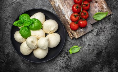 Peynir koleksiyonu, beyaz İtalyan peynirli mozzarella topları koyu bir arka planda taze fesleğen yaprakları ile servis ediliyor..