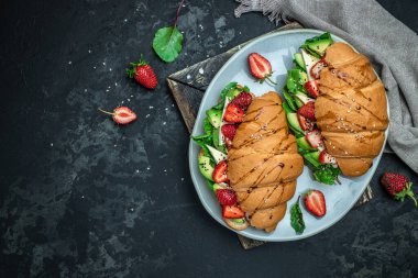 Avokado, çilekli, peynirli, peynirli kruvasan sandviçi susam ve kimyon serpiştirilmiş taze salata lezzetli kahvaltı veya atıştırmalık Keto diyet vejetaryen yemeği..