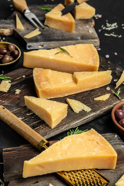 Parmesan cheese on a wooden board, Hard cheese, rosemary and cheese knife on a dark background. vertical image. top view.
