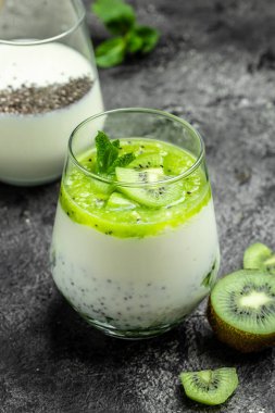 Sağlıklı kahvaltı pudingi, beyaz bir masada cam kavanozlarda kivi var. Temiz yemek, diyet, vejetaryen yemek konsepti. dikey resim.