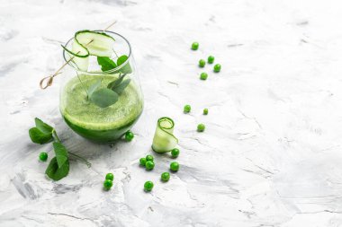 Açık beton arka planda bir bardakta salatalık yeşili smoothie. Detox smoothie, taze bezelye, salatalık, ıspanak ve limon. en üstteki görünüm.