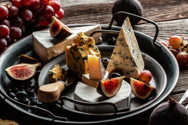 Çeşitli peynir çeşitleri, geleneksel Fransız parçaları, İtalyan ve İspanyol manchego peyniri üzümlü ve incirli ahşap masada servis edilmiş..