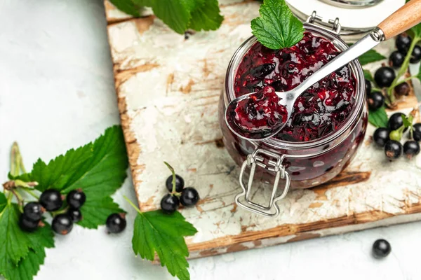 Black currant jam in a jar with fresh berry. Food recipe background. Close up,