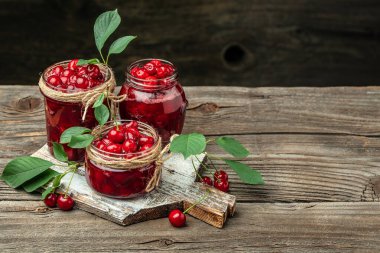 Bir kavanoz kiraz reçeli ve ekşi kiraz. Şerbetli kiraz. Olgun kirazlar. Tatlı kırmızı kirazlar. Ahşap bir arka planda konserve meyve.