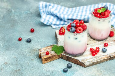 Ahududulu tatlı peynirli kek, ıvır zıvır, bardaktaki fare. Mavi arka planda ahududulu Yunan yoğurdu granola parfe. Restoran menüsü, diyet, yemek kitabı tarifi..