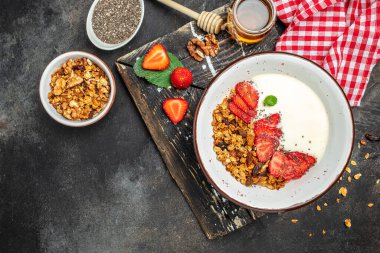 Yoğurtlu granola, taze çilek, chia tohumu ve bal, koyu arkaplanda. Lezzetli dengeli gıda konsepti. afiş, menü, metin için tarif yeri, üst görünüm.