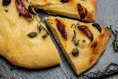 Focaccia ekmeği zeytinyağı, zeytin yağı, güneşte kurutulmuş domates, kapari ve kekik, koyu arkaplanda Akdeniz ekmeği. metin için yer.