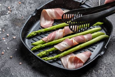 Kuşkonmaz ve pastırma. Jambona sarılı kuşkonmaz, arka planda ızgarada pişmeye hazır, yemek tarifi arka planında. Kapat.,