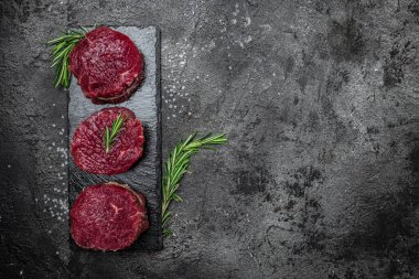Biberiye ve baharatlı sığır eti madalyonları koyu arkaplanda çiğ biftek fileto. afiş, menü, metin için tarif yeri, üst görünüm.