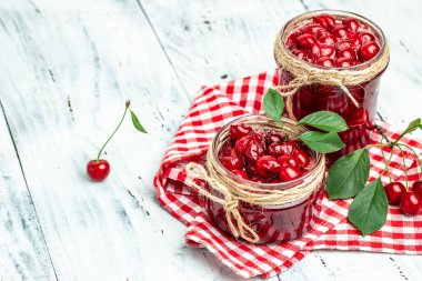 Bir kavanoz kiraz reçeli ve ekşi kiraz. Şerbetli kiraz. Olgun kirazlar. Tatlı kırmızı kirazlar. Ahşap bir arka planda konserve meyve.