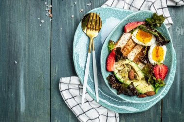 Sağlıklı besleyici paleo keto kahvaltı diyeti iki yumurta, avokado, ızgara tavuk fileto, fındık, çilek ve taze salata. Keto kahvaltısı ya da öğle yemeği. metin için yer, üst görünüm.