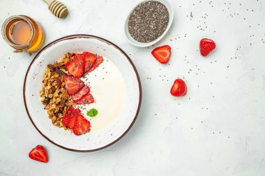 Yoğurtlu granola, taze çilek, chia tohumu ve bal beyaz arka planda. Lezzetli dengeli gıda konsepti. afiş, menü, metin için tarif yeri, üst görünüm.