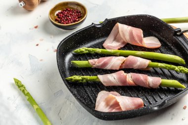 Asparagus and bacon. asparagus wrapped in ham ready for cooking on a grill pan on a light background, Food recipe background. Close up.