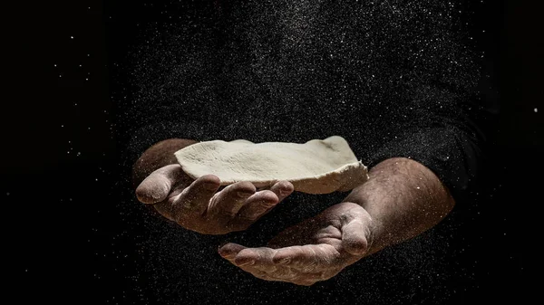 Beautiful and strong men's hands knead the dough make bread, pasta or pizza. Powdery flour flying into air. chef hands with flour in a freeze motion of a cloud of flour midair.