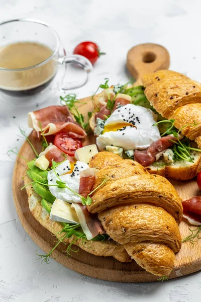 Spanish breakfast, Croissant Toast or sandwich with Poached egg, jamon, blue, cheese, avocado, microgin and cherry tomatoes, Cup of coffee, Food recipe background. vertical image.