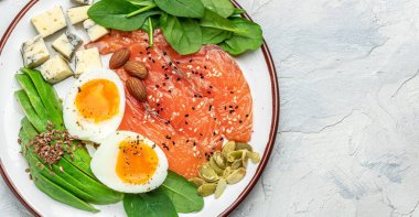 Keto diyet yemeği, somon, avokado, peynir, yumurta, ıspanak ve fındık. Ketojenik düşük karbonhidrat diyet konsepti. Sağlıklı yiyecekler için gerekli malzemeler. Uzun afiş biçimi. en üstteki görünüm.