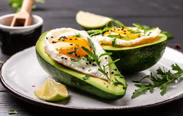 Avocado baked with eggs, fresh arugula, ground pepper on dark background, top view.