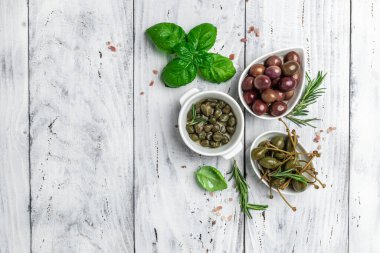 Marinated capers fresh basil leaves in a small bowl, on light wooden background. Long banner format. top view.