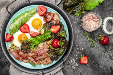 Keto diyet yemekli tabak. Yağda yumurta, pastırma, avokado, çilek ve taze salata. Keto kahvaltısı. metin için yer, üst görünüm.