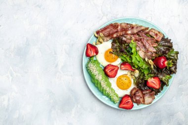 Ketojenik diyet yiyecekler, avokadolu kızarmış yumurta pastırması, çilek ve hafif arkaplanda taze salata. Sağlıklı yemek konsepti, uzun afiş formatı. en üstteki görünüm.