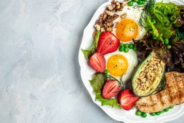 Ketogenic breakfast. Keto low carb Fried eggs, avocado, grilled chicken fillet, nuts, strawberries and fresh salad on a gray background. keto diet. Long banner format. top view.