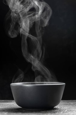Siyah arka planda pişirme kabı, sıcak yemek. Bir kase sıcak buhar dumanı, mutfak, yemek pişirme, konsept,