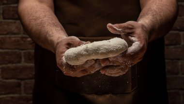 Güzel ve güçlü erkeklerin elleri hamuru yoğurarak ekmek, makarna ya da pizza yaparlar. Bir un bulutu toz gibi uçuşuyor. Yiyecek konsepti.