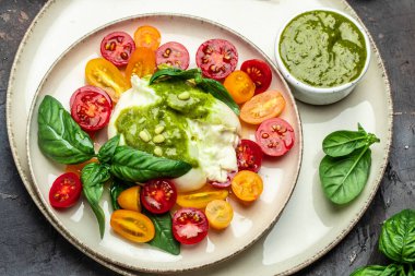 Salad burrata cheese tomatoes and green pesto. Delicious balanced food concept. superfood concept. Healthy, clean eating. Vegan or gluten free diet. top view.
