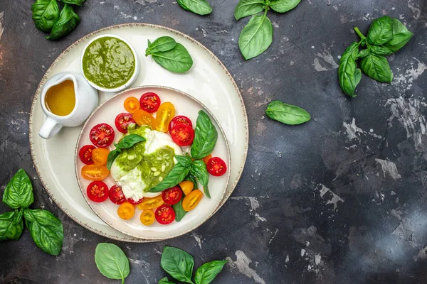 Salad with Tomatoes and Burrata cheese and green pesto on a dark background. banner, menu, recipe place for text, top view.