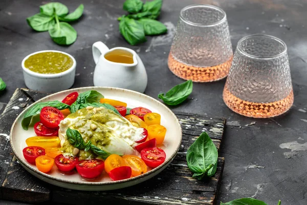 Traditional Italian dish burrata cheese with glass of rose wine. Burrata served with tomatoes and green pesto. place for text, top view.