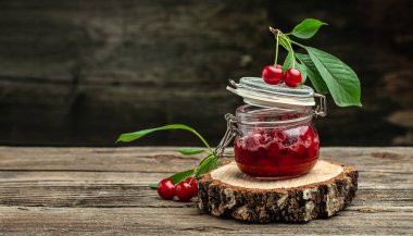 Ahşap arka planda taze kırmızı kiraz meyvesi. Bir kavanoz kiraz reçeli ve ekşi kiraz. Şerbetli kiraz. Konserve meyve. metin için yer, üst görünüm.