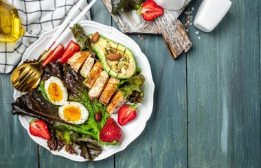 Ketojenik düşük karbonhidrat diyeti. Keto yiyecekli tabak: iki yumurta, avokado, ızgara tavuk fileto, fındık, çilek ve taze salata. Sağlıklı yağlar, kilo vermek için temiz yiyecekler. görünüm.