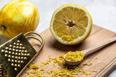 Peeling lemon rind to add zest to Mediterranean recipes. Grater peel and lemon zest on light background, top view.