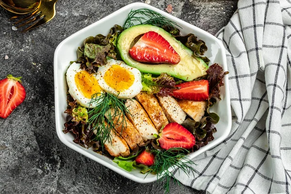 Sağlıklı besleyici paleo keto kahvaltı diyeti iki yumurta, avokado, ızgara tavuk fileto, fındık, çilek ve taze salata. Keto kahvaltısı ya da öğle yemeği. metin için yer, üst görünüm.
