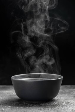 Siyah arka planda kaynayan ot, sıcak yemek konsepti. Bir kase sıcak dumanlı çorba.,