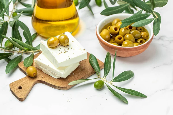 Feta cheese with olives and green herbs and olive oil sauce in bowl on light background. place for text, top view.