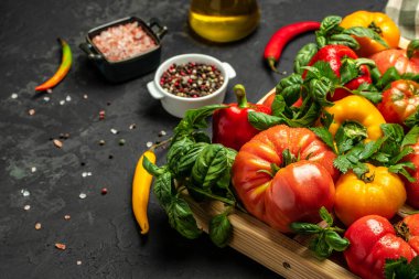 Çeşitli renkli bahçe domatesleri, dolmalık biber ve baharatlar. Karanlık arka planda yemek pişirmek için gerekli malzemeler. metin için yer, üst görünüm.