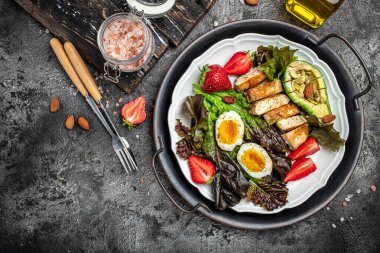 Ketogenic breakfast. Keto low carb Fried eggs, avocado, grilled chicken fillet, nuts, strawberries and fresh salad on a gray background. keto diet. Long banner format. top view.