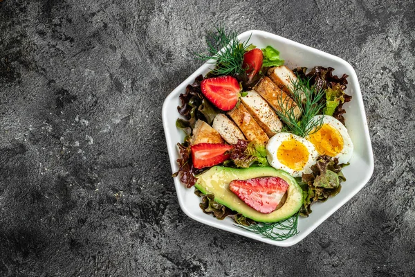 Ketogenic low carbs diet. Plate with keto foods: two eggs, avocado, grilled chicken fillet, nuts, strawberries and fresh salad. Healthy fats, clean eating for weight loss. view.