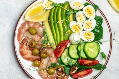 Ketojenik diyet kahvaltı karidesleri, karidesler, yağda yumurta, taze salata, domates, salatalık ve avokado. Keto, paleo yemeği. üstte.
