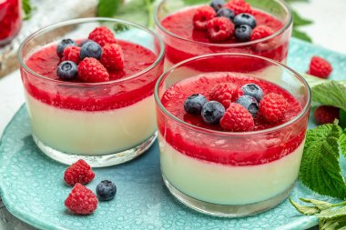 Ahudududulu panna cotta, üzerinde ahududu reçeli ve koyu bir arka plan. Küçük kavanozlarda krema soslu böğürtlen tatlısı. metin için yer.