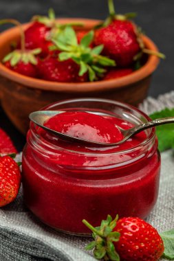 Cam kavanozda çilek reçeli ve karanlık masa kaşığı. dikey görüntü. en üstteki görünüm,